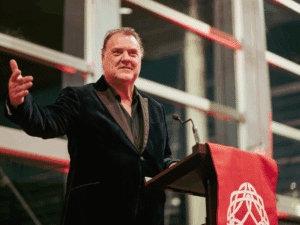 Bryn Terfel standing at a lectern with the Learned Society of Wales logo, delivering a speech.