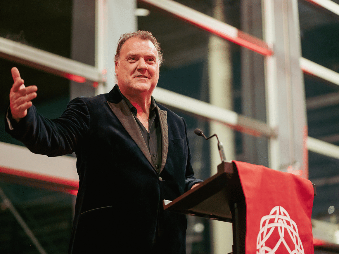 Bryn Terfel standing at a lectern with the Learned Society of Wales logo, delivering a speech.