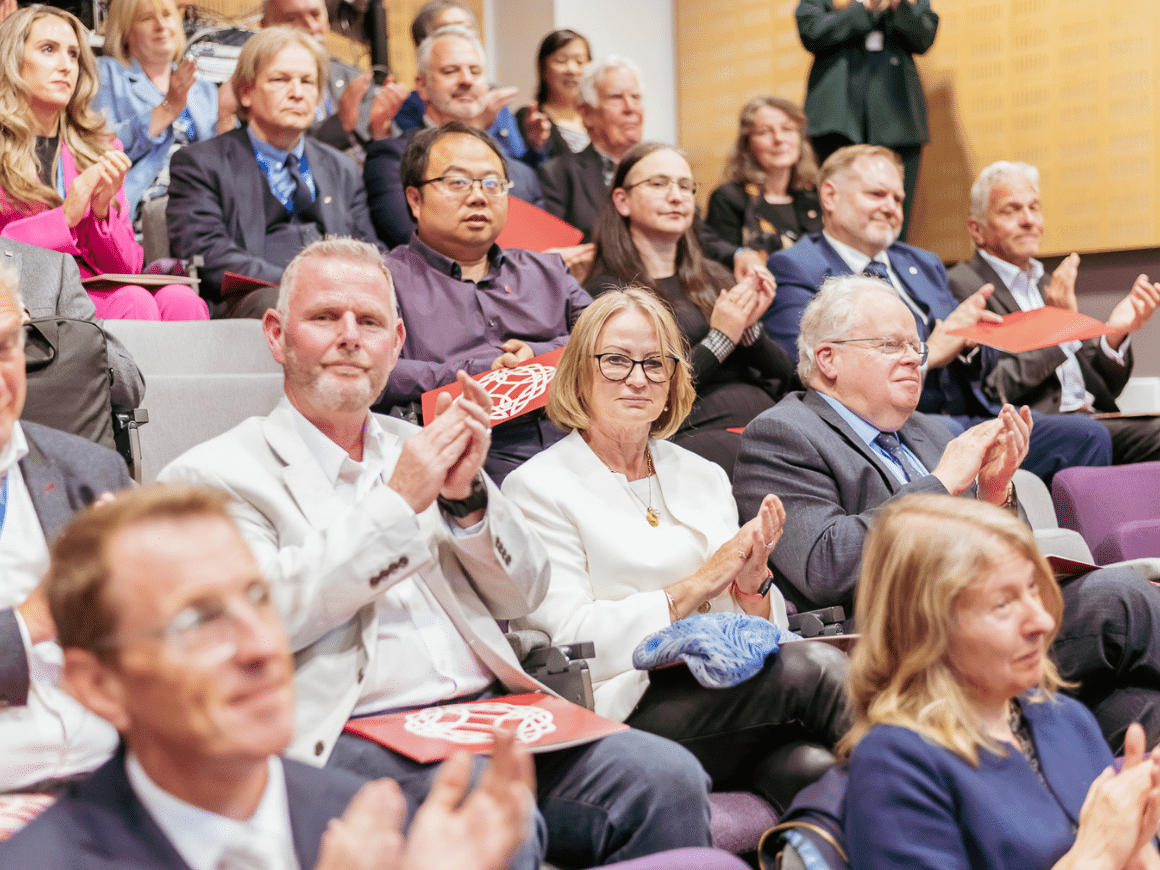 A group of people sitting in the tiered seats of a lecture hall, applauding.