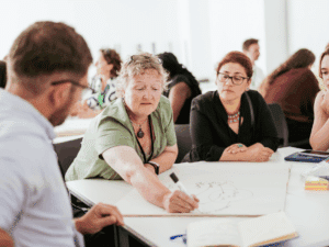 Three women and a man sitting around a table as one writes with a marker pen on a large sheet of paper.