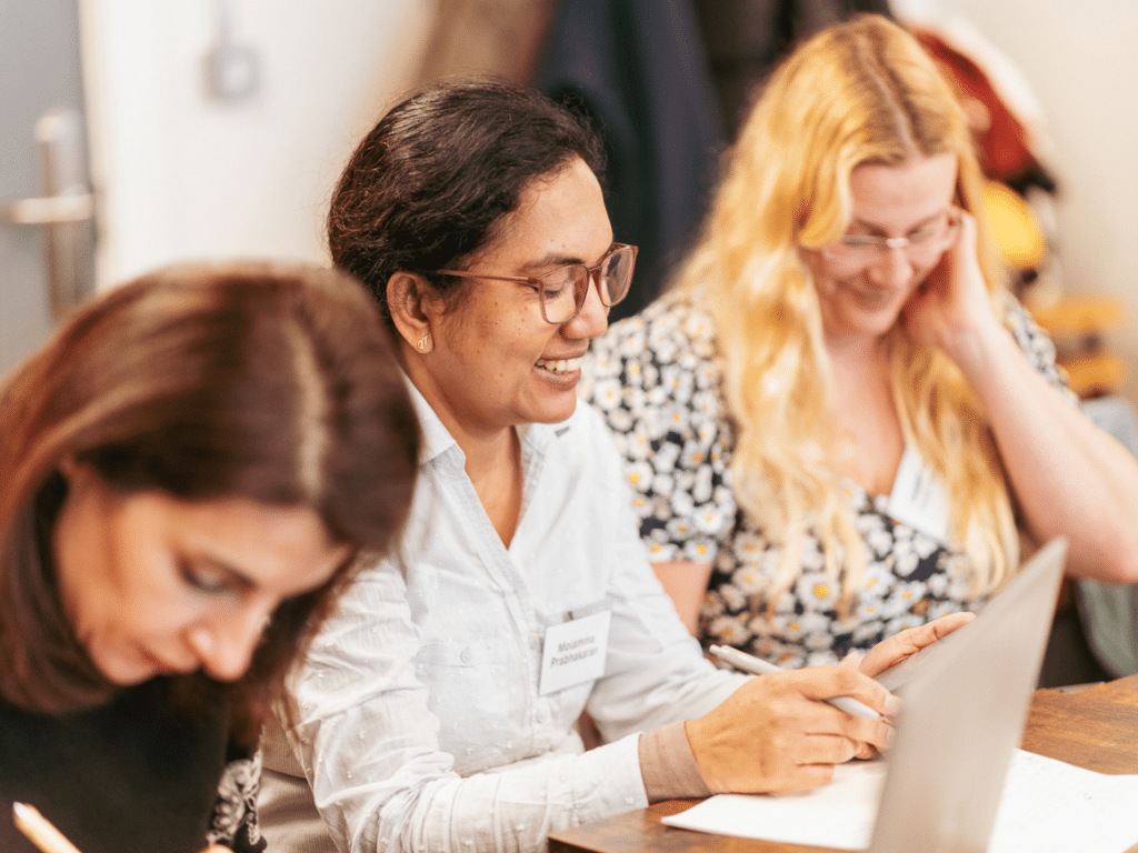 Three women at a table with a laptop and some papers in front of them.