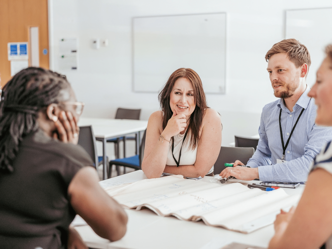 Four people, three women, one man, in discussion around a table with a flipchart in front of them.