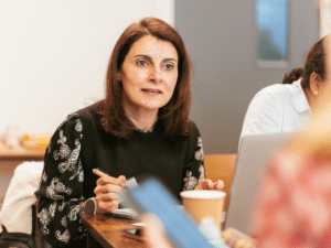A woman holding a pen leaning forward and listening intently to someone off camera.
