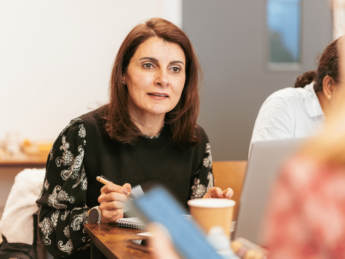 A woman holding a pen leaning forward and listening intently to someone off camera.