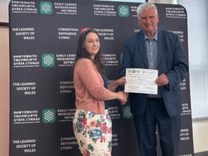 A man and woman shaking hands while he presents her with a certificate.