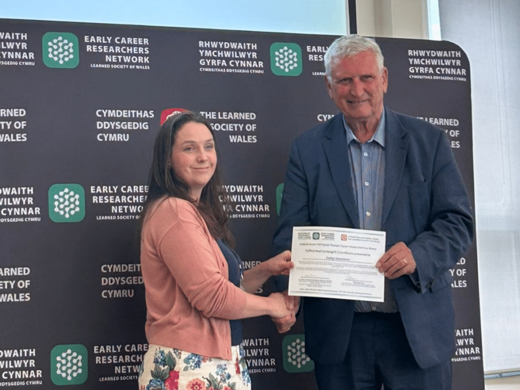 A man and woman shaking hands while he presents her with a certificate.