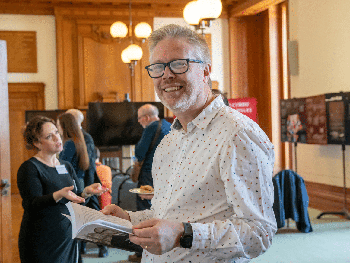 A man holding a brochure smiles directly at the camera.