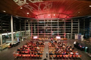 The inside of the Senedd with rows of seats in the main hall and a man talking at a lectern.